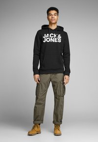 Black hoodie with "JACK & JONES" logo, paired with olive cargo pants and tan work boots. The hoodie features a front pocket and drawstrings.