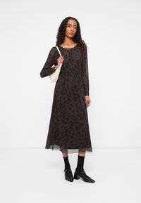 Pruun läbipaistev maksikleit musta loomapritiga, pikkade varrukatega ja kogutud vöökoht. Kaasatud mustade pahkluute rihmadega kingade ja valge käekotiga.