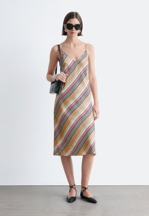 Kvinde iført solbriller og en ærmeløs, stribet midi-kjole med sorte flade sko og en sort skuldertaske.