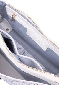 Interno di una borsa bianca con foderatura azzurro chiaro, dotata di tasche con zip e tasche a scomparsa. Hardware dorato e motivo stampato visibile all'esterno.