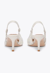 Witte hielsandalen met bloemenpatroon, open zijkanten en slanke hakken. Voorzien van een enkelbandje en een tan leren binnenzool. Minimalistisch ontwerp.