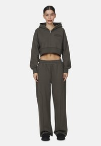 Olijfgroen cropped hoodie met capuchon en rits, gecombineerd met bijpassende losse joggingbroek met contrasterende naden en een elastische tailleband.