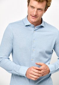 Camicia azzurro chiaro a maniche lunghe con un tessuto testurizzato, dotata di colletto appuntito e cinque bottoni frontali. Vestibilità morbida e informale.
