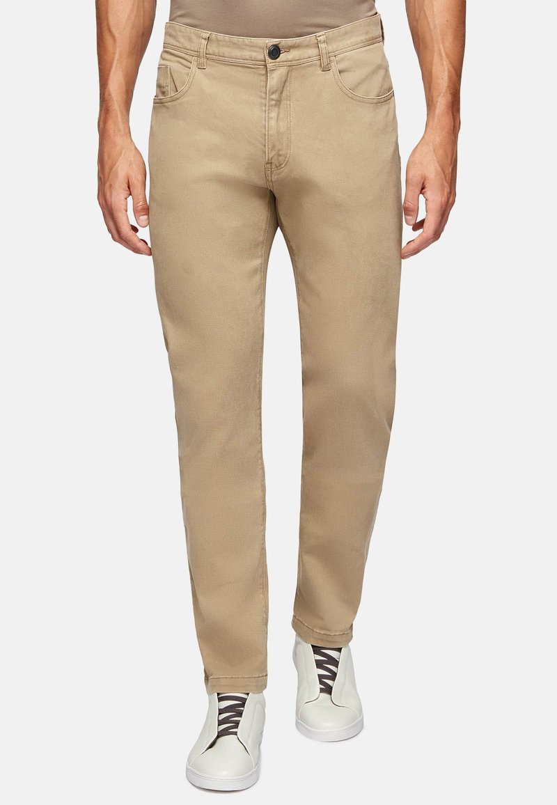 Beige cotton pants with a straight fit, five-pocket design, belt loops, and a button closure, paired with white slip-on shoes.