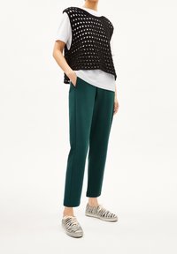 Un haut noir en maille ouverte superposé sur une chemise blanche, associé à un pantalon vert ajusté et des baskets à imprimé zèbre. Caractéristiques : coupe décontractée et poches.