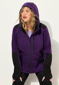 Giacca in fleece viola con cappuccio, caratterizzata da dettagli neri, tasche con zip e tessuto testurizzato. Dettaglio cucito sulle spalle.