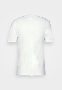 Camiseta blanca de manga corta hecha de algodón, con cuello redondo y dobladillo recto. La parte trasera presenta una costura que corre verticalmente.