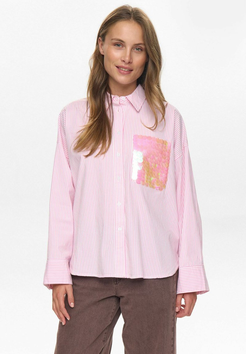 Roze en witte gestreepte blouse met lange mouwen en een zak met paillettenaccent. De stof heeft een gladde textuur; de kraag staat rechtop.