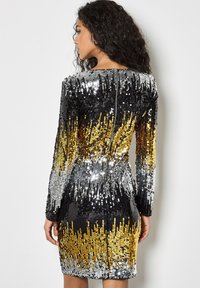 Vestido de manga larga con un degradado de lentejuelas en negro, plateado y dorado, con una silueta ajustada y un cierre de cremallera en la parte posterior.