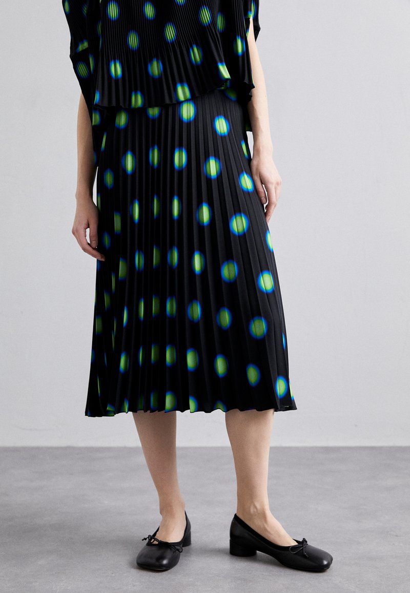 Black pleated skirt with blue and green circular patterns, paired with black shoes featuring a small heel and decorative bow accents.
