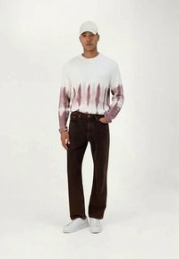 Suéter blanco con estampado tie-dye y degradado púrpura, pantalones marrones, zapatillas blancas y una gorra clara. Atuendo casual con corte holgado y textura suave.