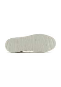 Suela de zapatilla de color claro con un patrón texturizado y el distintivo logo "ARMANI" moldeado en la goma, con un perfil plano.