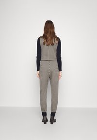 Combinaison à carreaux avec un motif noir et blanc, coupe ajustée, dotée d'un haut ajusté et de poignets. Stylée avec des bottines noires.