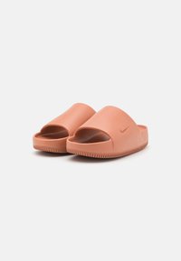 Nike-sandaalit persikanvärisenä, avonaisella kärjellä, sileällä pinnalla ja kuviollisella pohjalla. Sivussa on pieni logo.