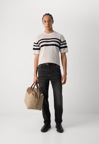 Weißes gestricktes T-Shirt mit schwarzen Streifen, dunkle Denim-Jeans, schwarze Schuhe und eine braune Tasche mit braunen Akzenten und doppeltem Reißverschluss.