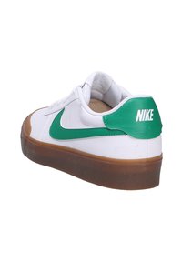 Witte Nike sneaker met een groene swoosh en hielaccent. Voorzien van een rubberen gumzool. Subtiele stiksels en een gewatteerde kraag voor comfort.