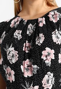 Czarny materiałowy top z różowymi kwiatowymi wzorami i białymi kropkami. Marszczony dekolt z krótkimi rękawami, zapewniający luźne dopasowanie.