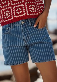 Shorts en denim avec des rayures verticales bleues et blanches, un ourlet effiloché, des poches standard et une taille classique avec une fermeture à bouton.