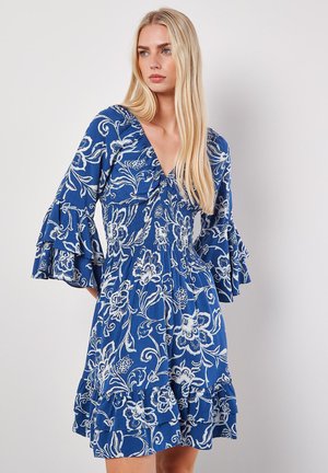 Blaues Blumenkleid mit weißen Mustern, V-Ausschnitt, Glockenärmeln und gestuftem Rüschensaum. Hergestellt aus leichtem Stoff.