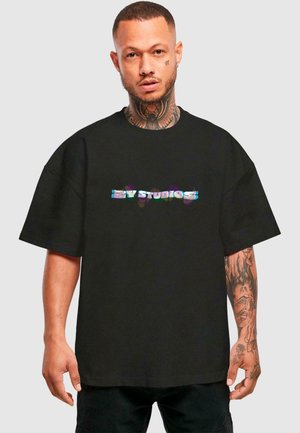 Sort oversized t-shirt med korte ærmer, prydet med et holografisk "BY STUDIOS" logo på brystet. Blødt bomuldsstof.