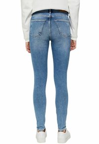 Jeans ajustados en denim azul claro, con una cintura de altura media, cinco bolsillos y una textura suave; combinados con zapatillas blancas.
