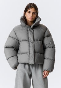 Šedá prešívaná bunda so skráteným strihom, vybavená vysokým golierom, prešívanými sekciami a hladkou, lesklou textúrou. Vhodná do chladného počasia.