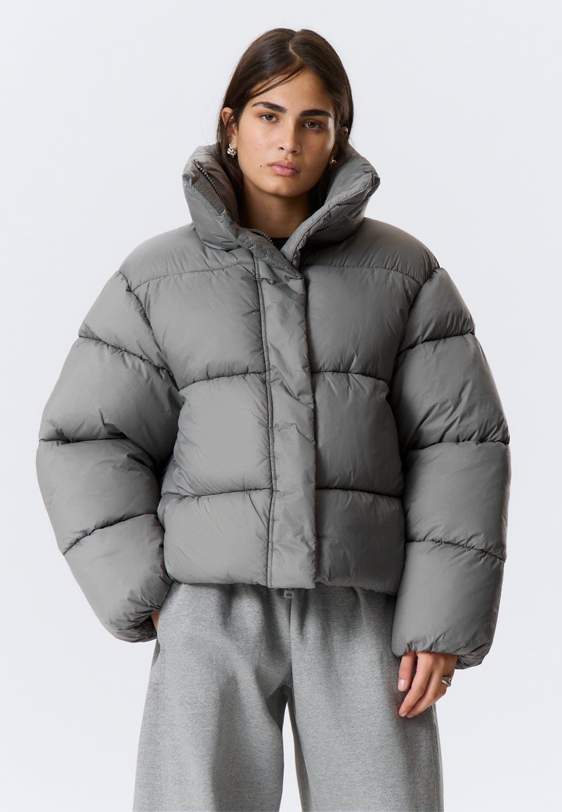Šedá prešívaná bunda so skráteným strihom, vybavená vysokým golierom, prešívanými sekciami a hladkou, lesklou textúrou. Vhodná do chladného počasia.