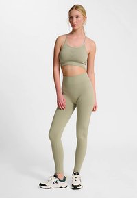 Olivgrönt träningsset med en figurnära sport-bh och högmidjade leggings, tillverkade av ett mjukt, elastiskt material. Vita träningsskor ingår.