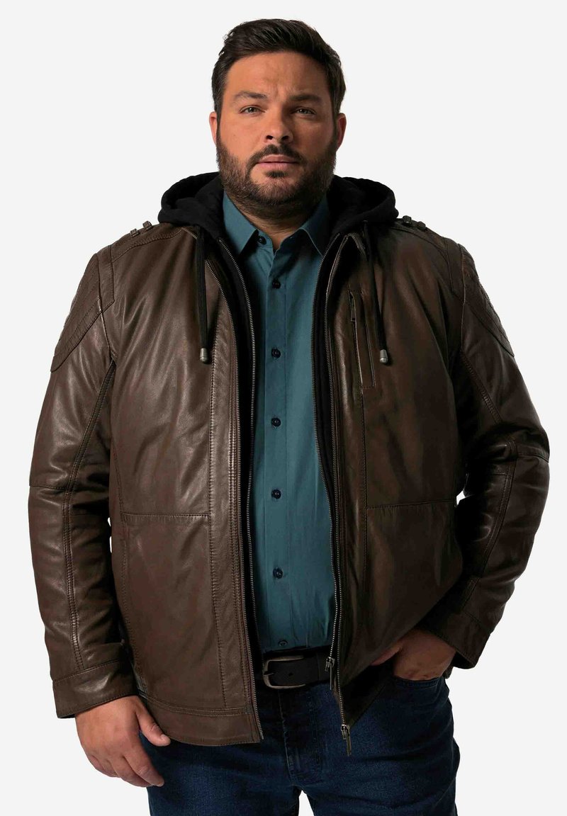 Chaqueta de cuero marrón con capucha negra, con cierre frontal, bolsillos y detalles en los hombros. Llevada sobre una camisa de botones en tono verde azulado.