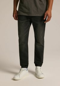 Czarne spodnie dresowe z elastycznymi mankietami, wykonane z denimu. Połączone z białymi sneakersami, charakteryzującymi się minimalistycznym designem i jasnymi akcentami kolorystycznymi.