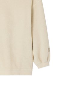 Pull beige en polaire à manches longues avec poignets et ourlet côtelés, tissu doux texturé, et détail de texte subtil sur la partie inférieure de la manche.