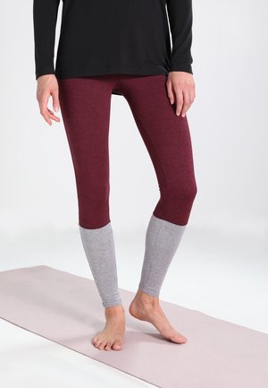 Leggings burdeos con paneles inferiores grises, hechos de una tela elástica, que presentan un ajuste ceñido y una textura suave, mostrados con una blusa negra.