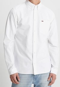 Wit overhemd met lange mouwen en een klassieke kraag, voorzien van een borstzak en een klein logo-accent. Gladde katoenen stof, reguliere pasvorm.