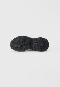 Talpa unei pantofi sport negri, cu un model texturat, striații adânci și caneluri asimetrice pentru o aderență și tracțiune îmbunătățite.