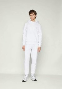 Vit huvtröja med framficka, vita tapered sweatpants och vita sportskor. Slät tygkvalitet, avslappnad passform, minimalistisk design.