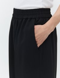 Hand resting inside the side pocket of black elastic-waist pants worn with a white top against a plain background.