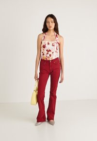 Halterneck-toppi, jossa valkoinen pohja ja punaisia sekä vaaleanpunaisia kukkakuoseja. Yhdistetty korkeavyötäröisiin punaisiin leveälahkeisiin farkkuihin ja keltaiseen käsilaukkuun.