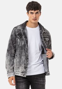 Zwarte en grijze denimjack met een vervaagd ontwerp, twee borstzakken, knoopsluiting en contrasterende binnenvoering. Model draagt een wit T-shirt.