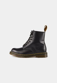 Botte noire en cuir jusqu'à la cheville avec bout rond, texture lisse, couture jaune, six œillets et une languette au talon. Semelle épaisse.