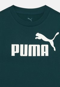 Tmavě zelené bavlněné tričko s velkým bílým logem "PUMA" a bílou grafikou skákající pumy nad textem. Klasický design s kulatým výstřihem.