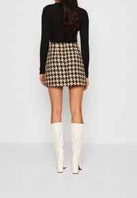 Černý top s dlouhým rukávem spárovaný s béžovou a černou kostkovanou mini sukní, doplněný bílými vysokými podpatky.