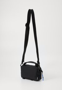 Black crossbody bag made of textured fabric, featuring a detachable strap, top handle, and a zipper closure with a blue accent.
