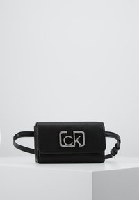 Czarna skórzana torebka o teksturowanym wykończeniu, z metalicznym logo z przodu i odczepianym paskiem, co umożliwia wszechstronne noszenie.