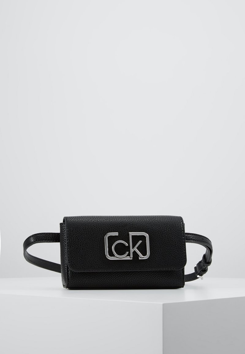 Czarna skórzana torebka o teksturowanym wykończeniu, z metalicznym logo z przodu i odczepianym paskiem, co umożliwia wszechstronne noszenie.