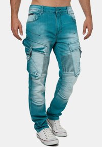 Pantalons cargo bleu clair en denim, avec des accents côtelés, de multiples poches et une coupe décontractée, associés à des baskets blanches.