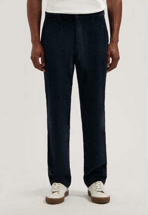 Marineblauwe corduroy broek met een recht model, voorzien van verticale ribbels en voorzakken, gecombineerd met witte sneakers.