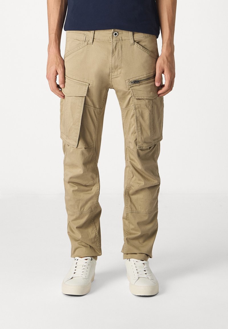Khaki cargo kalhoty s několika kapsami, mírně zúženými nohavicemi a hladkým materiálem z bavlněné směsi. Obsahují zipovou kapsu a zapínání na knoflík.