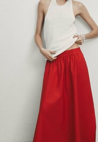 Haut halter tricoté blanc associé à une jupe rouge fluide arrivant au genou, dotée d'une taille élastique pour le confort et la facilité de port.