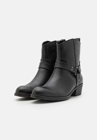 Bottines noires en cuir synthétique texturé, avec une sangle décorative ornée de détails en métal et un petit talon empilé.