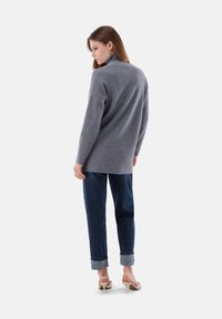 Grauer, langärmeliger Pullover mit hohem Kragen, kombiniert mit dunkelblauen Jeans mit hochgekrempelten Säumen und beigen High-Heels. Weiche Textur.